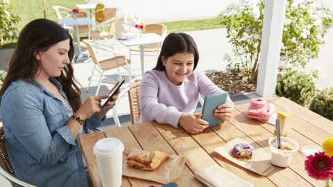 Mother and daughter sitting at outdoor dining table viewing their own devices. 