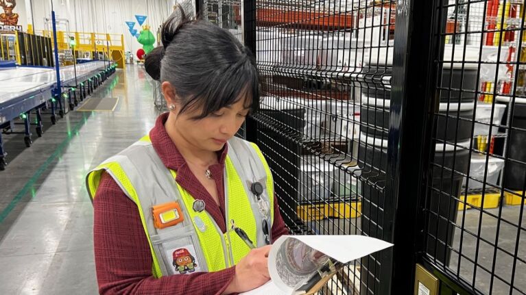 An image of a woman dressed in a yellow work vest holding a clipboard.