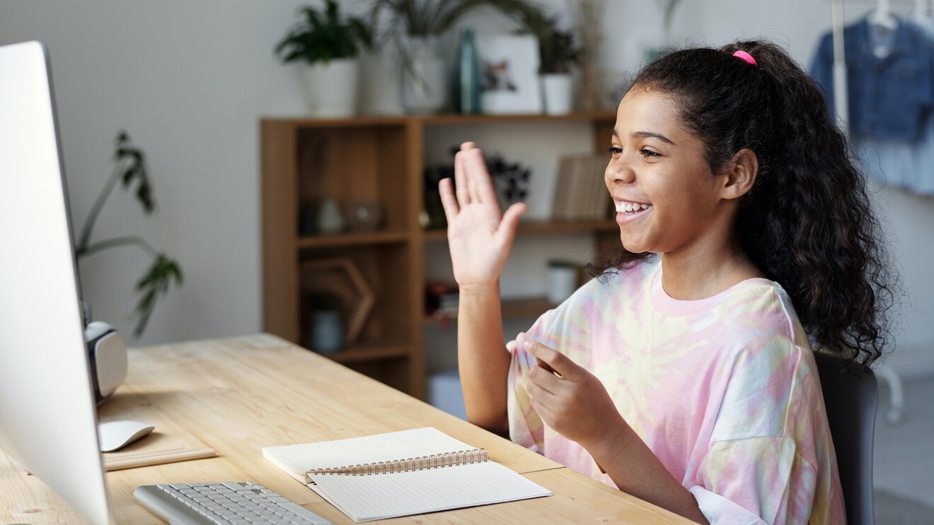 A young woman waves at her computer monitor as sheparticipates in a video chat. 