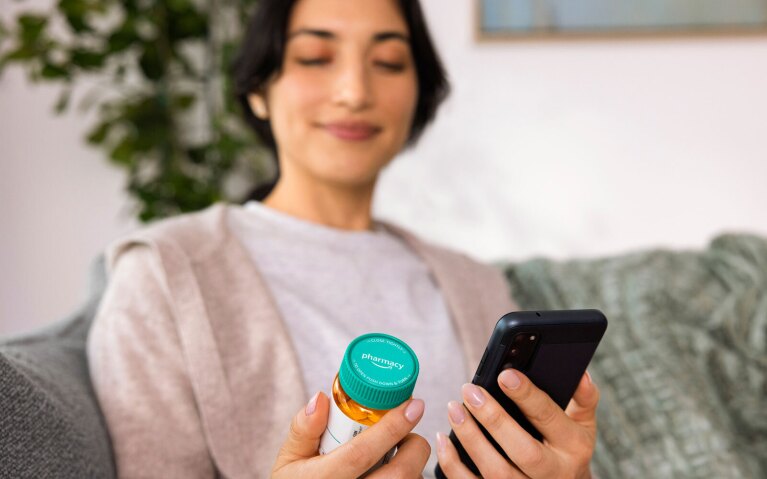 An image of a person holding a phone and an Amazon Pharmacy prescription bottle. 