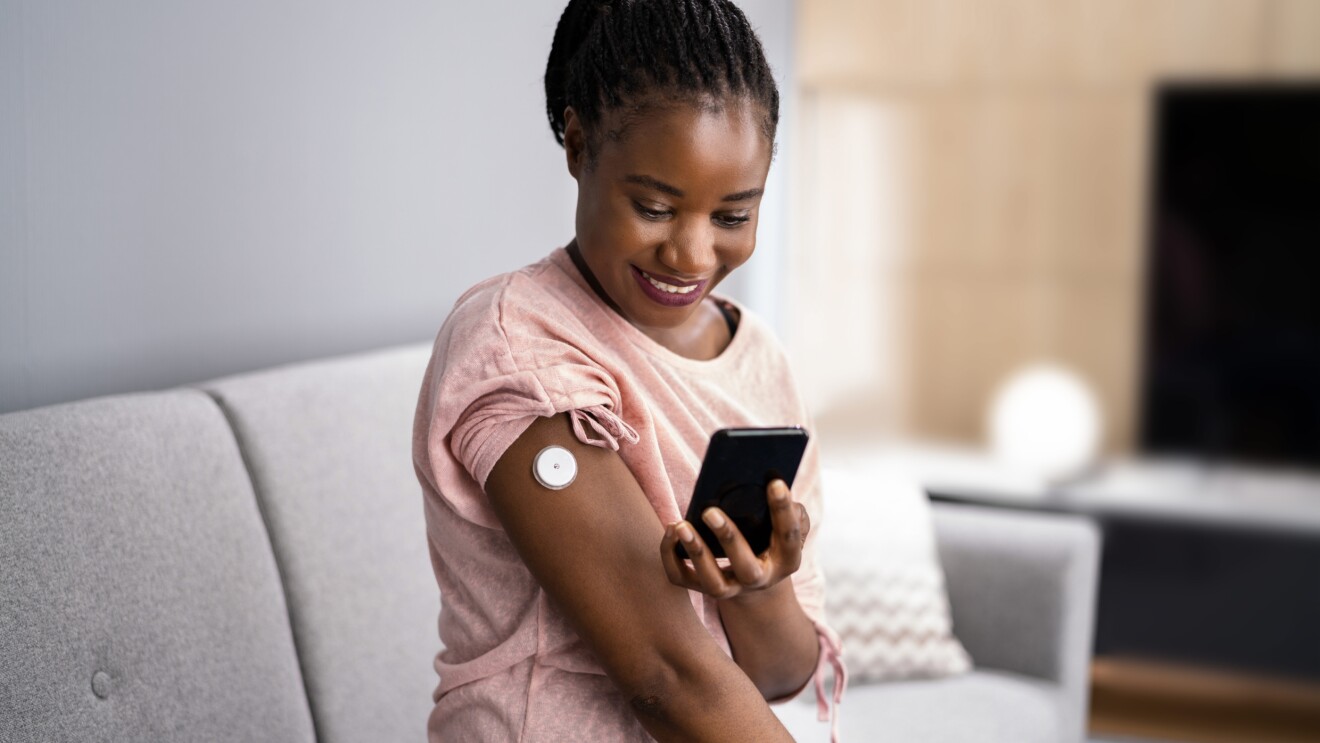 An image of a woman using a patch on her arm and looking at her phone. 