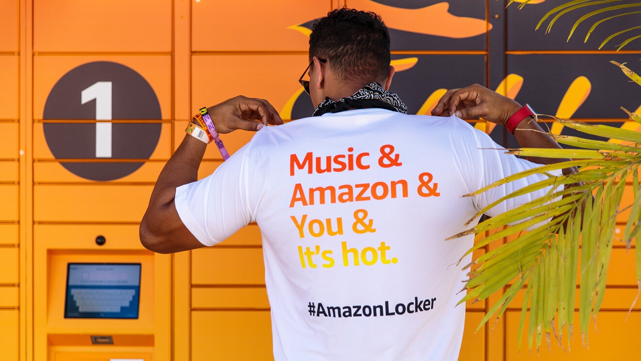 A man wearing a white t-shirt with a message of "Music & Amazon & You & It's hot" printed on the back. He pulls up on the shoulders of the tee as though he's fanning himself. 