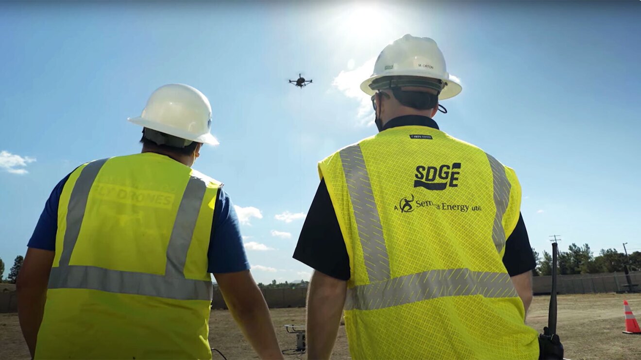 An image of two men looking up at the sky at a drone in the air.