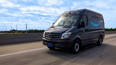 A cargo van decorated with the Amazon smile logo and the word "Prime" drives down the road.