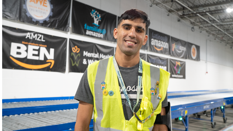 An Amazon employee wears a yellow safety vest and smiles in a fulfillment center.