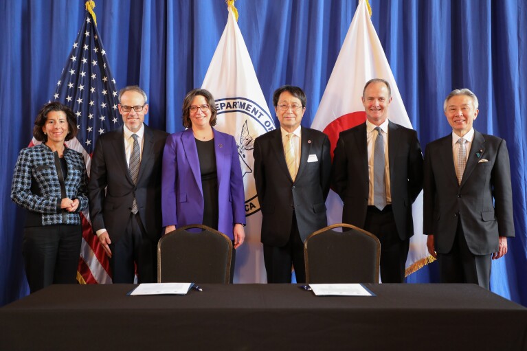 A photo of (left to right) Gina Raimondo, U.S. Secretary of Commerce, David Zapolsky, senior vice president, Global Public Policy & General Counsel, and four representatives from participating organizations at the U.S. Department of Commerce in Washington, D.C. standing on stage in front of a table to sign for an AI partnership.