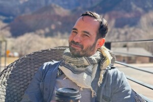 Chief Meteorologist Victor Rodriguez holds a coffee in his hands as he sits in a chair near the base of mountains.