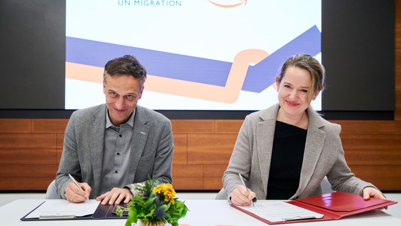 Representatives from Amazon and IOM sign an agreement and shake hands.