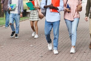 Image of five students holding school supplies walking through campus.