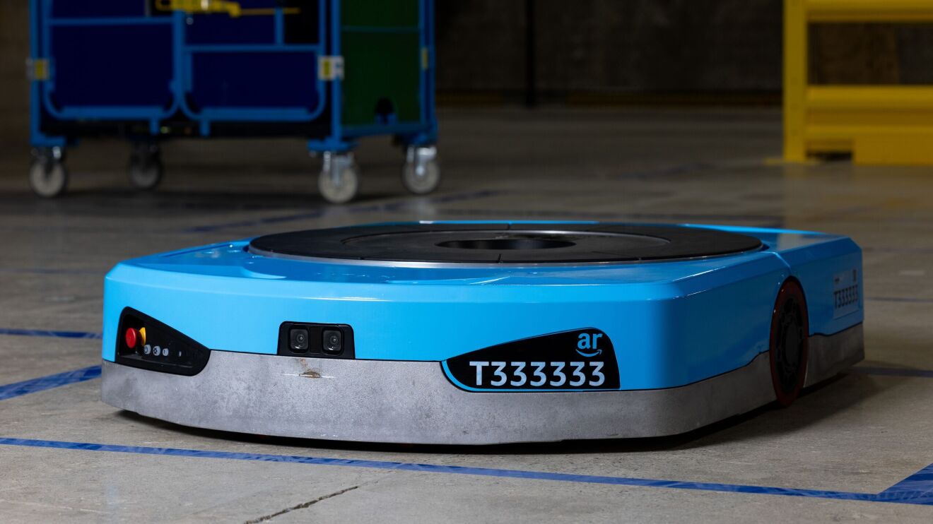 An image of Amazon's new Titan robot. It's blue, plate-like robot with black details, including a camera on the front, a name plate that says "T333333" and a large, circular plate on top. 