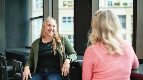 Two woman engage in a conversation with each other in an Amazon office. 