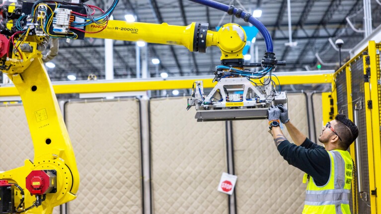 A photo of an Amazon employee working on a robot in a warehouse. 