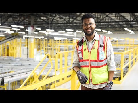 An image of Abdiaziz, an area manager working in an Amazon fulfillment center, wearing a yellow safety vest and gloves.