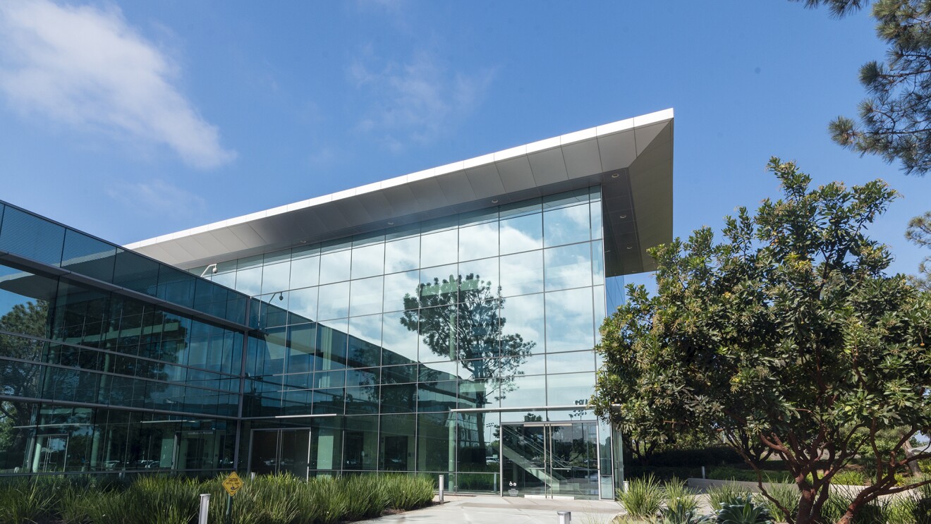 The exterior of a building, built of reflective glass, surrounded by grasses and trees.