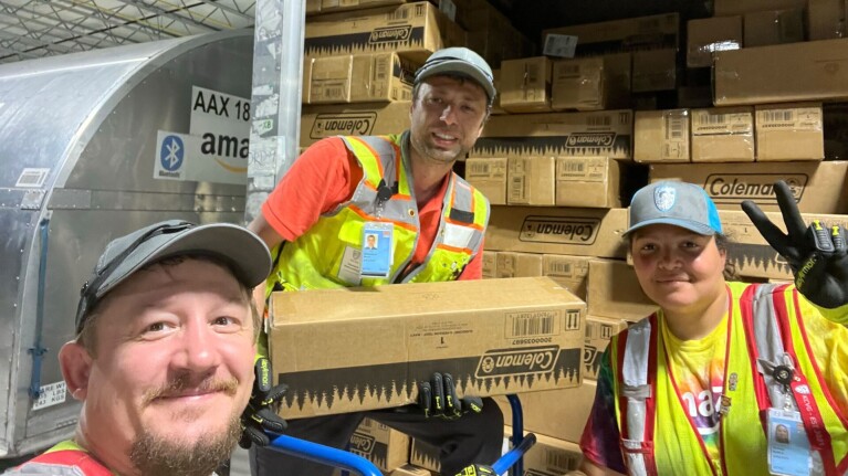 Three Amazon employees package up relief items and load them into a delivery truck.