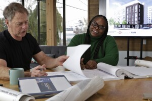 A photo of two people sitting at a desk reviewing blueprints. 