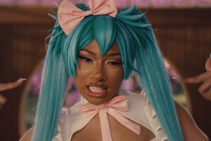 A close-up image of Megan Thee Stallion dressed in a blue wig with pigtails and a pink bow. 