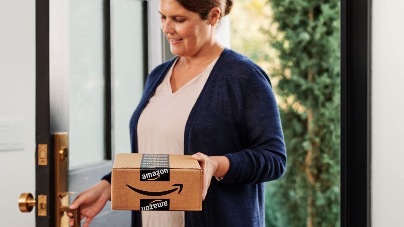 An image of a person opening a front door holding an Amazon delivery box. 